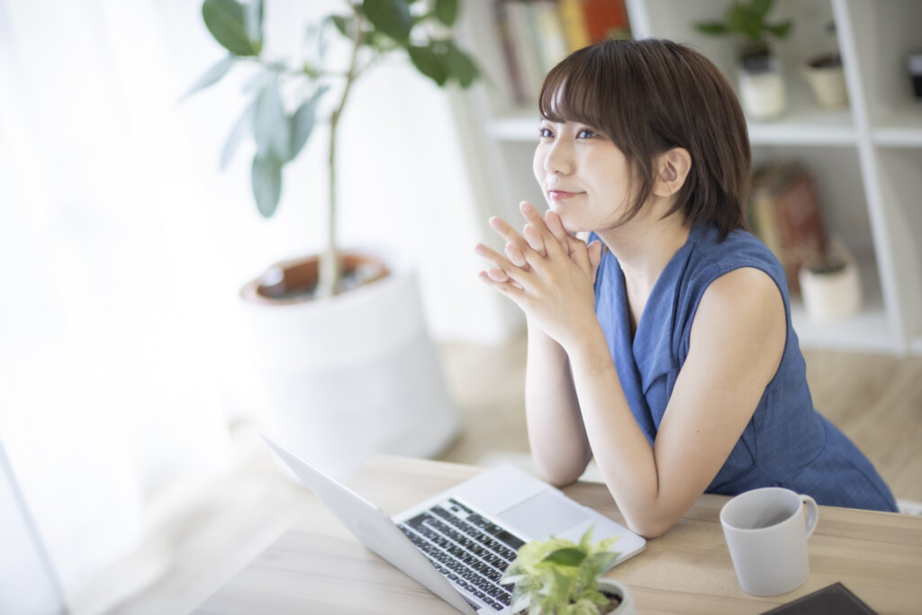 パソコンの前で笑顔で考え事をする女性