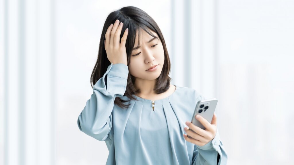 スマートフォンを見て悩む女性